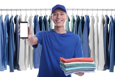 Image of Dry-cleaning delivery. Happy courier holding folded clothes and smartphone near wardrobe rack on white background