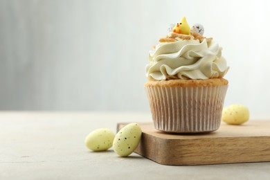 Tasty Easter cupcake with vanilla cream and candies on gray table, space for text