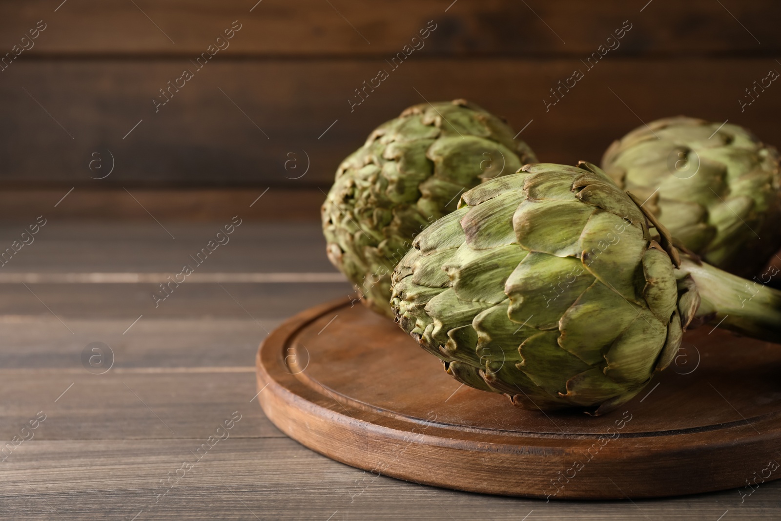 Photo of Fresh raw artichokes on wooden table, space for text
