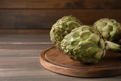 Photo of Fresh raw artichokes on wooden table, space for text