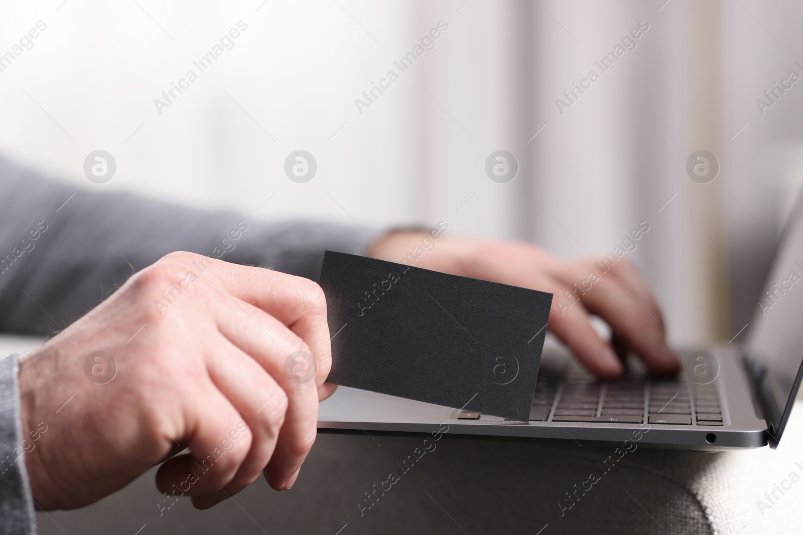 Photo of Man with laptop holding blank business card on blurred background, closeup