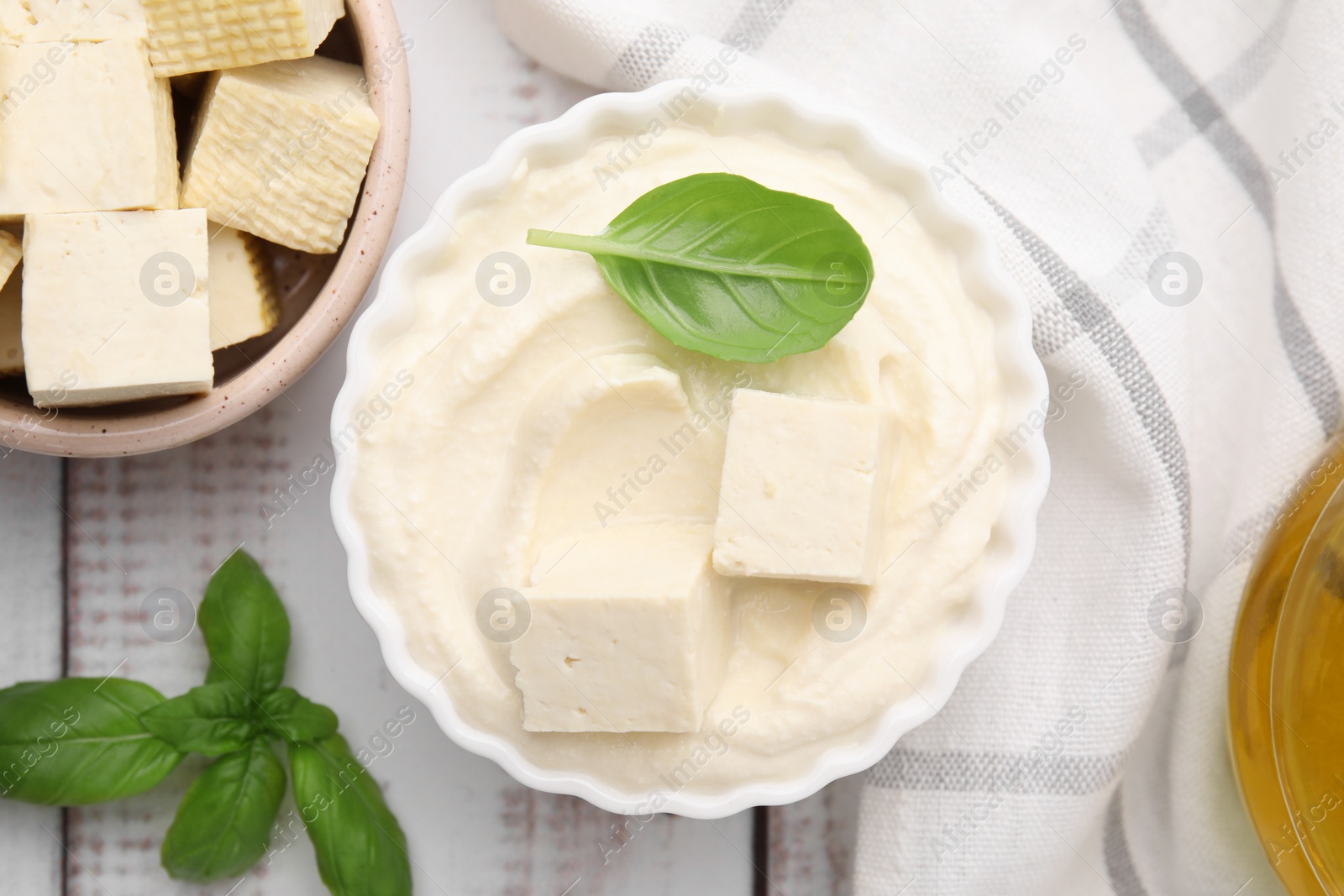 Photo of Delicious tofu sauce and basil leaves on white wooden table, flat lay