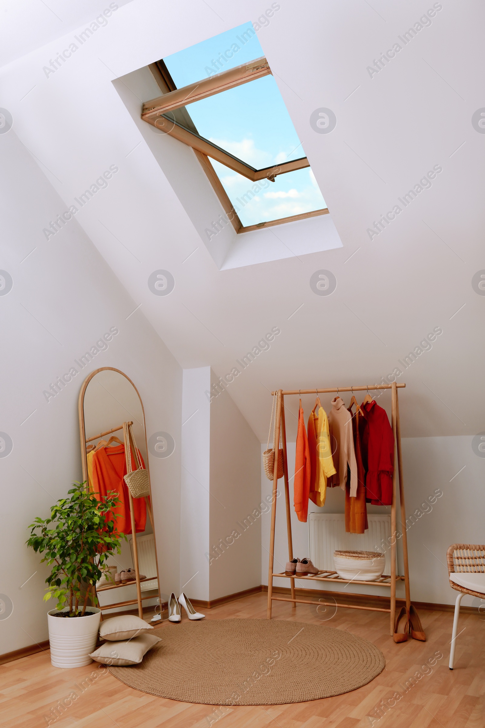 Photo of Stylish clothes rack, mirror and wicker chair in attic room. Interior design