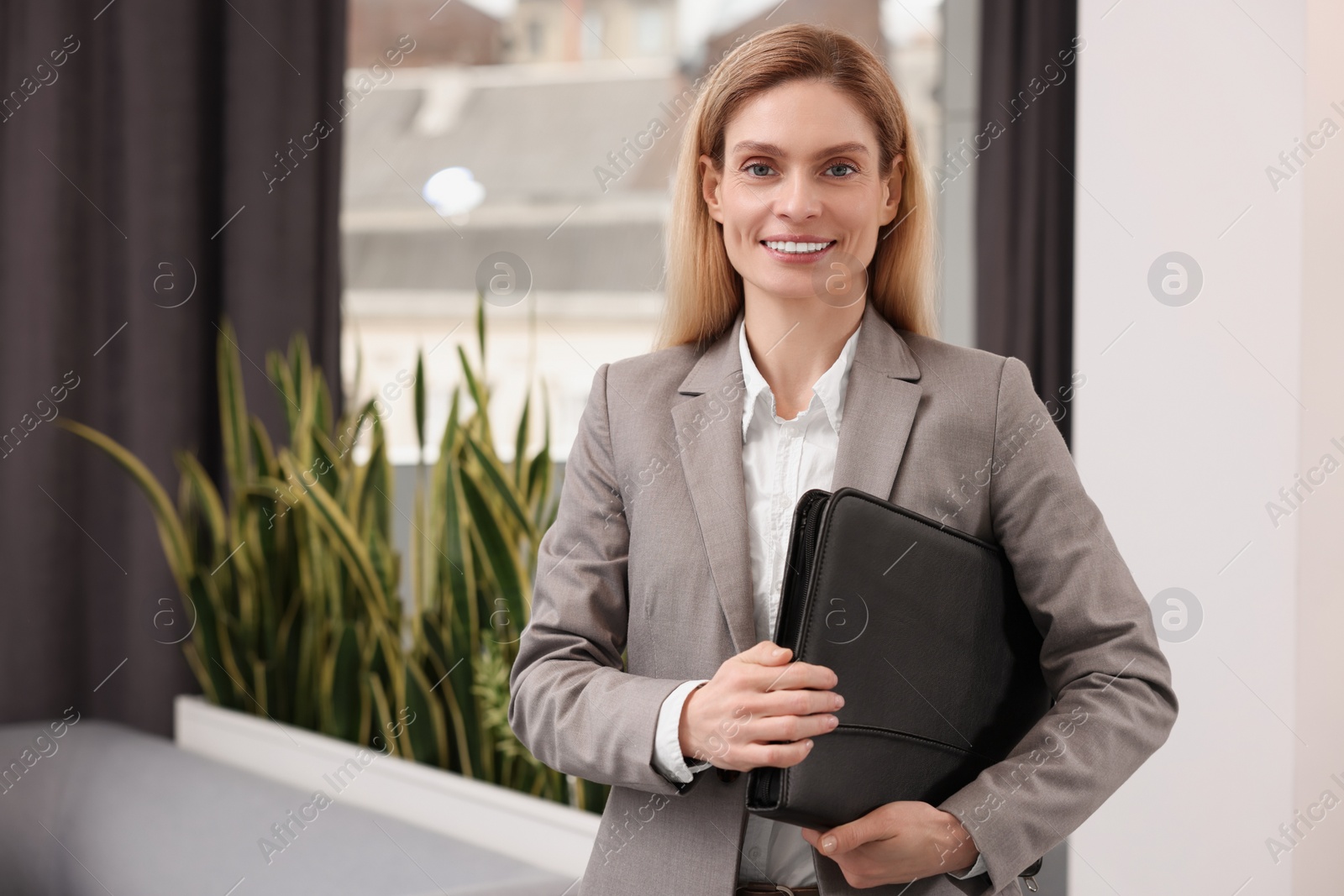 Photo of Happy real estate agent with leather portfolio indoors. Space for text