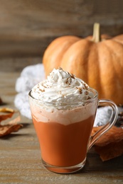 Photo of Pumpkin spice latte with whipped cream in glass cup on wooden table