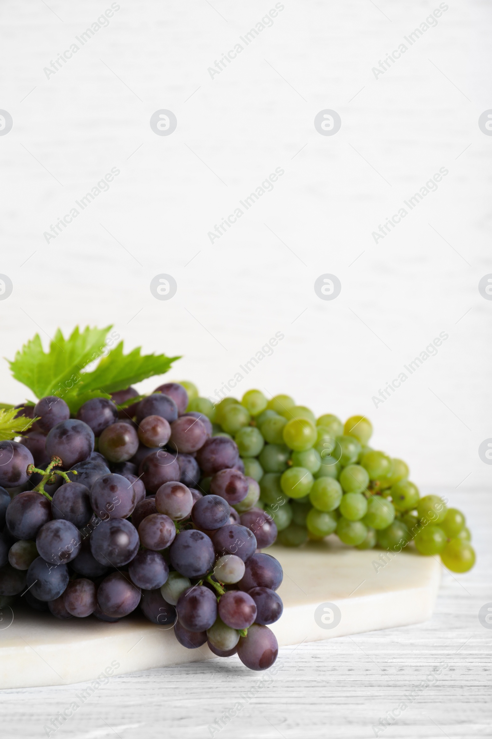 Photo of Fresh ripe juicy grapes on white wooden table, space for text