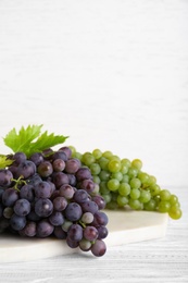 Photo of Fresh ripe juicy grapes on white wooden table, space for text