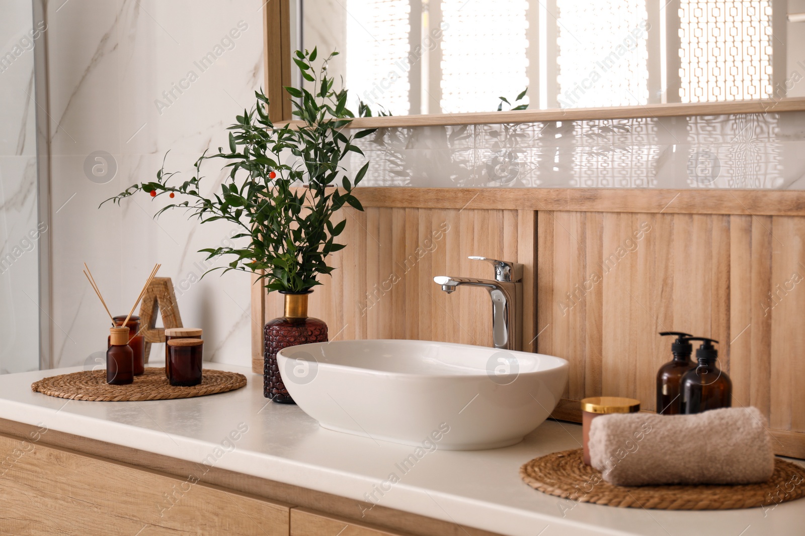 Photo of Vase with beautiful branches, candles and air reed freshener near vessel sink in bathroom. Interior design