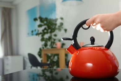 Woman holding modern kettle on stove in kitchen, closeup with space for text