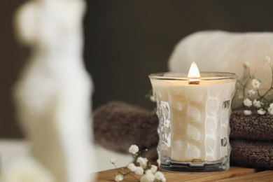 Photo of Beautiful burning candle and gypsophila flowers on wooden table in room, closeup