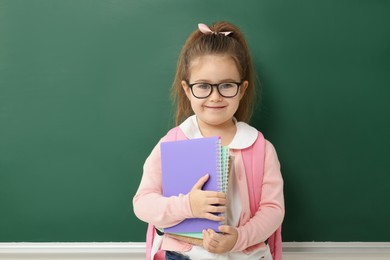 Photo of Happy little school child with notebooks near chalkboard