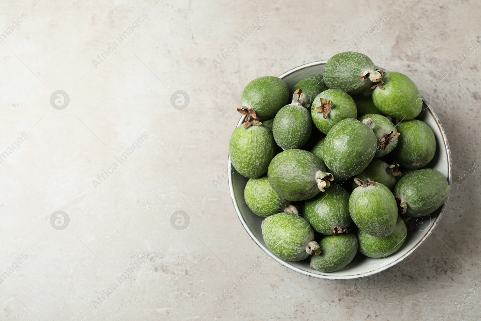 Photo of Fresh green feijoa fruits in bowl on light grey table, top view. Space for text