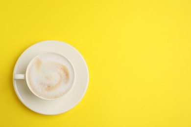 Tasty cappuccino in coffee cup on yellow background, top view. Space for text