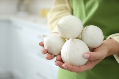 Woman holding white onions indoors, closeup view