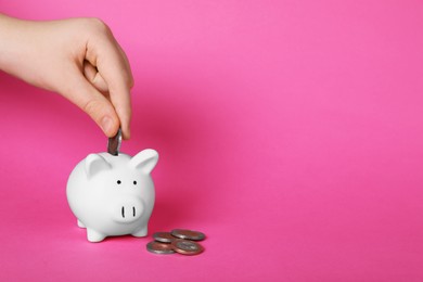 Woman putting coin into ceramic piggy bank on pink background, closeup with space for text. Financial savings