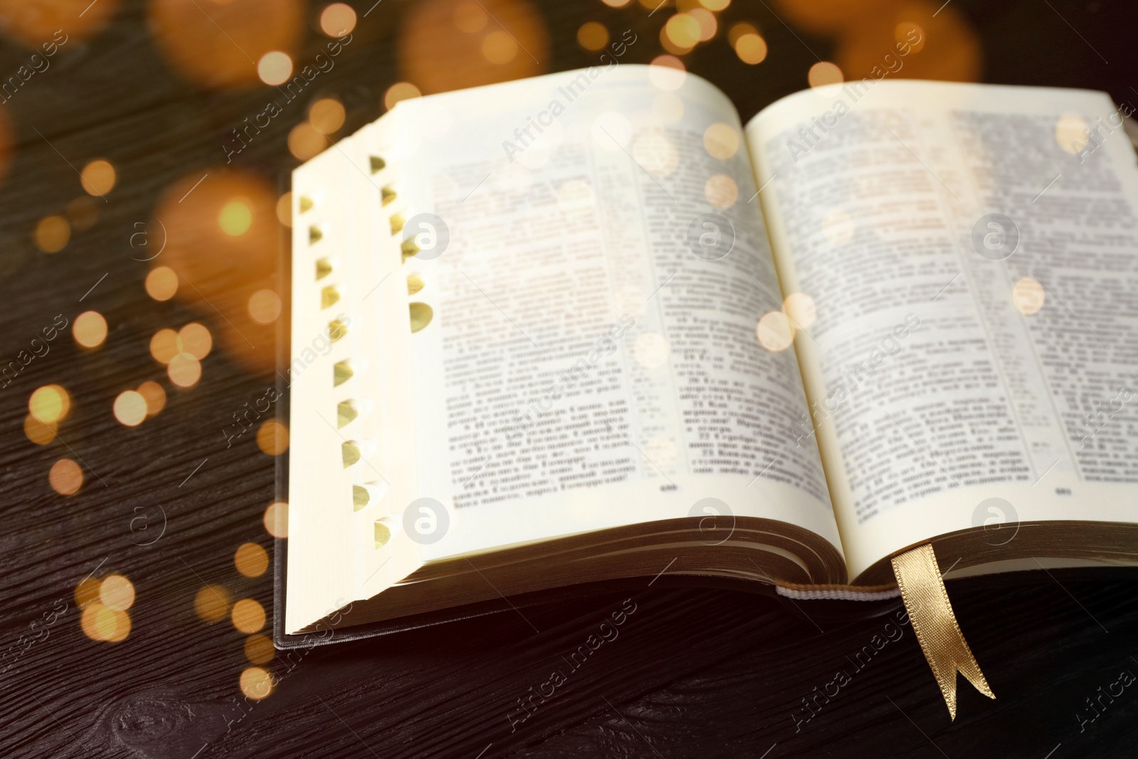 Image of Open Bible on black wooden table, bokeh effect