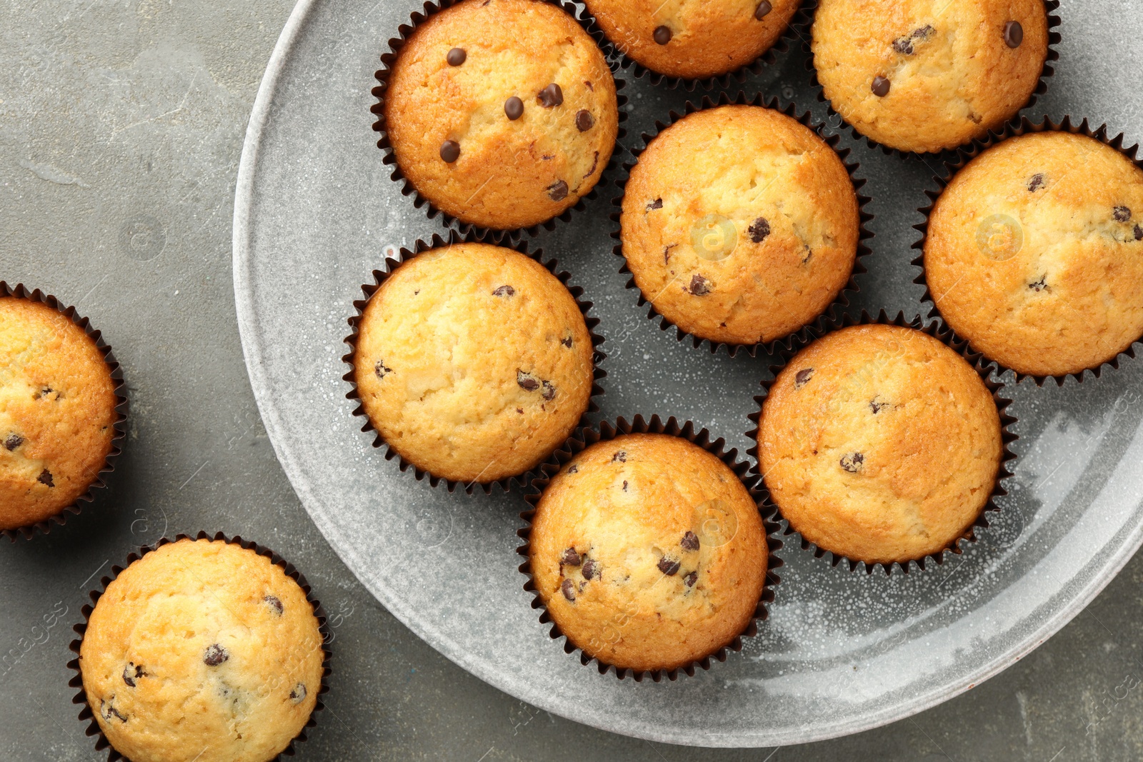 Photo of Delicious freshly baked muffins with chocolate chips on gray table, top view