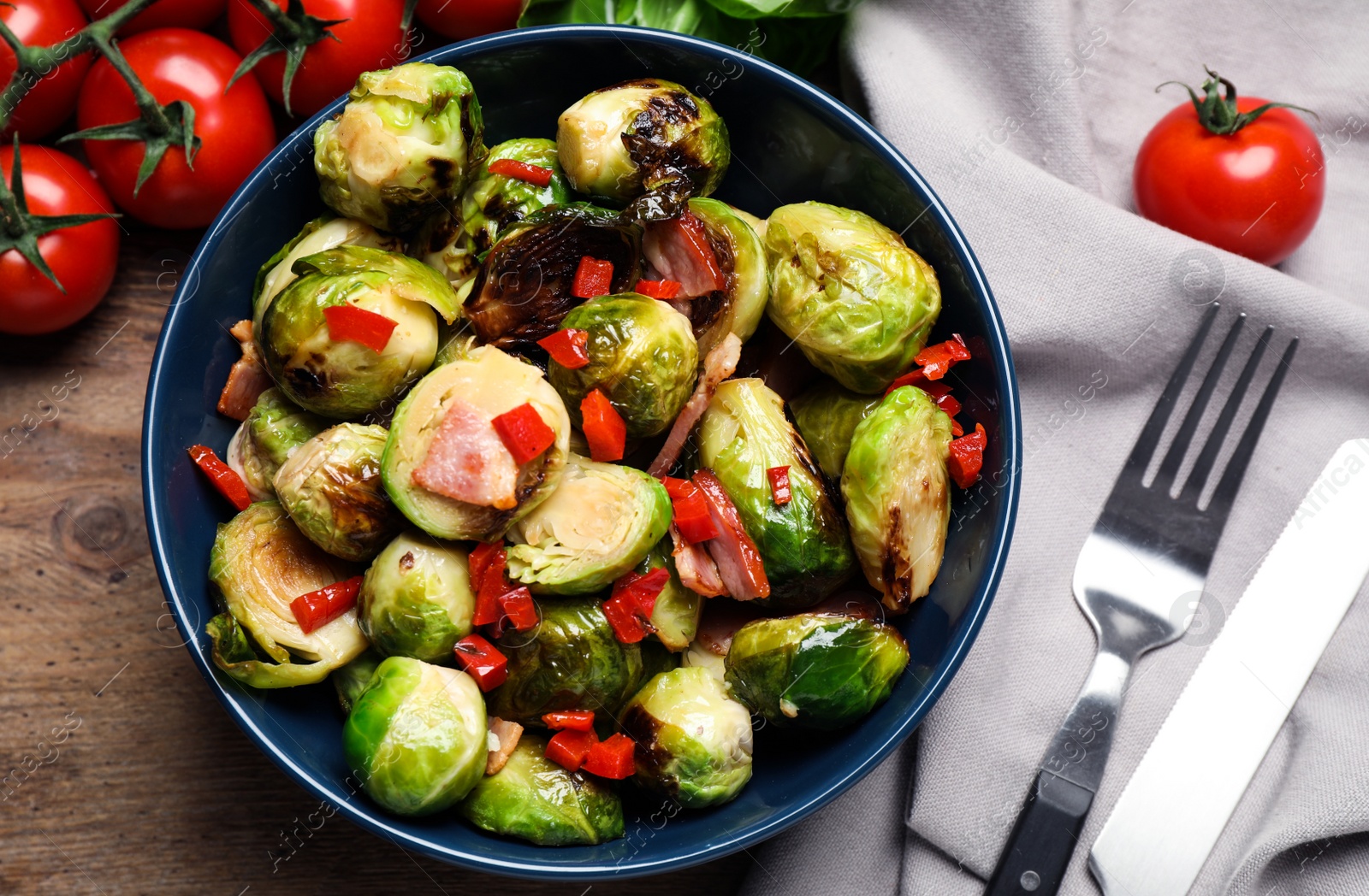 Photo of Delicious Brussels sprouts with bacon in bowl on wooden table, flat lay