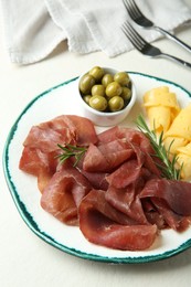 Photo of Delicious bresaola, cheese, olives and rosemary on light textured table