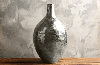 Stylish silver ceramic vase on wooden table against grey background