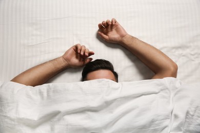 Man sleeping under soft blanket in bed at home, top view
