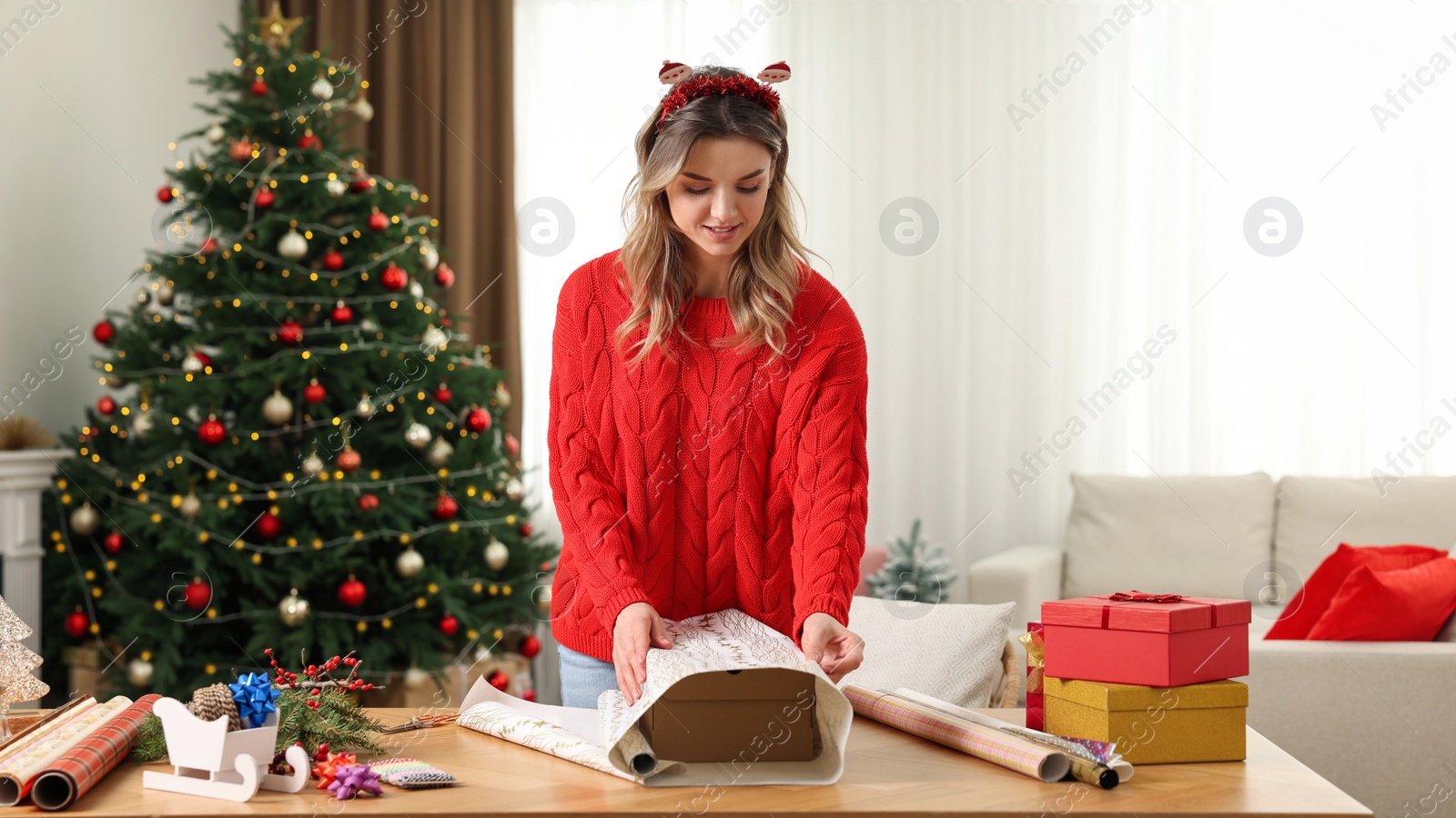 Photo of Beautiful young woman wrapping Christmas gift at home