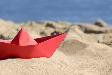 Photo of Red paper boat near sea on sunny day, closeup. Space for text