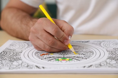 Photo of Man coloring antistress picture at table indoors, closeup