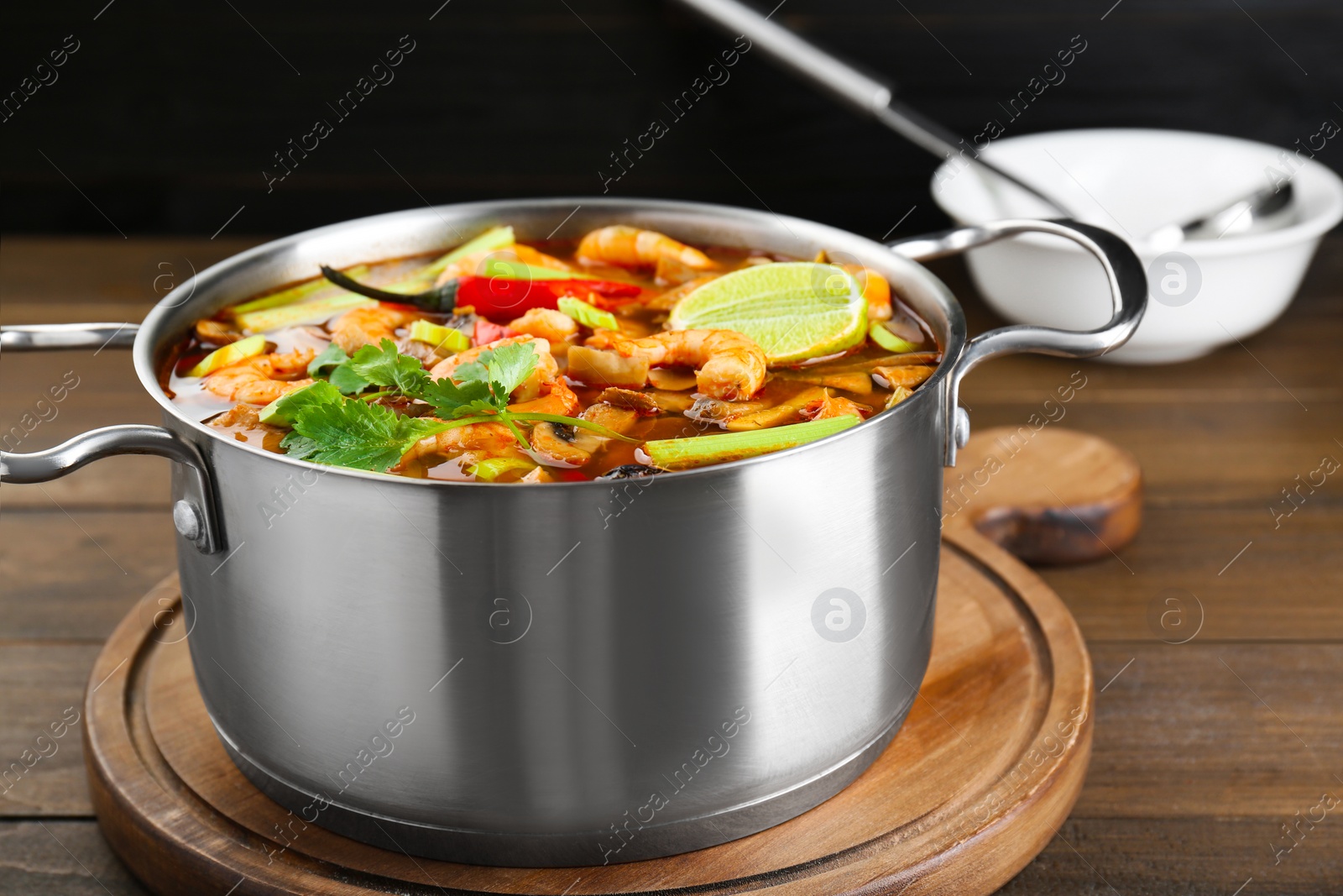 Photo of Saucepan with delicious Tom Yum soup on wooden table