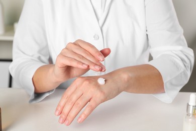 Photo of Dermatologist testing cosmetic product at white table indoors, closeup