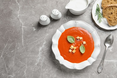 Photo of Fresh homemade tomato soup served with bread on grey table, top view. Space for text