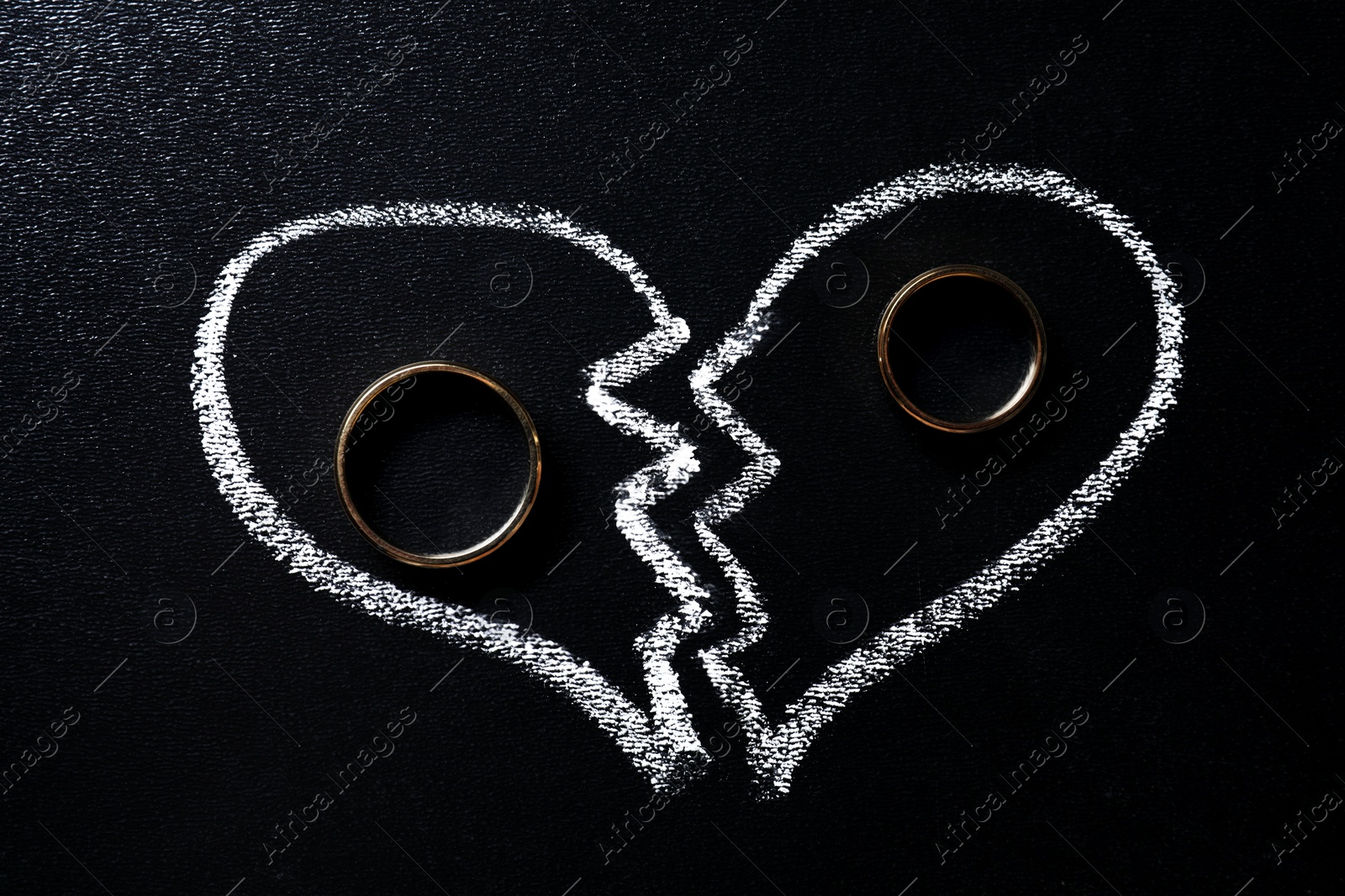 Photo of Divorce concept. Wedding rings and broken heart drawn on blackboard, flat lay