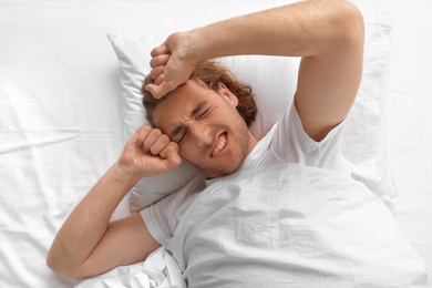 Photo of Handsome young man stretching while lying on pillow in morning, top view. Bedtime