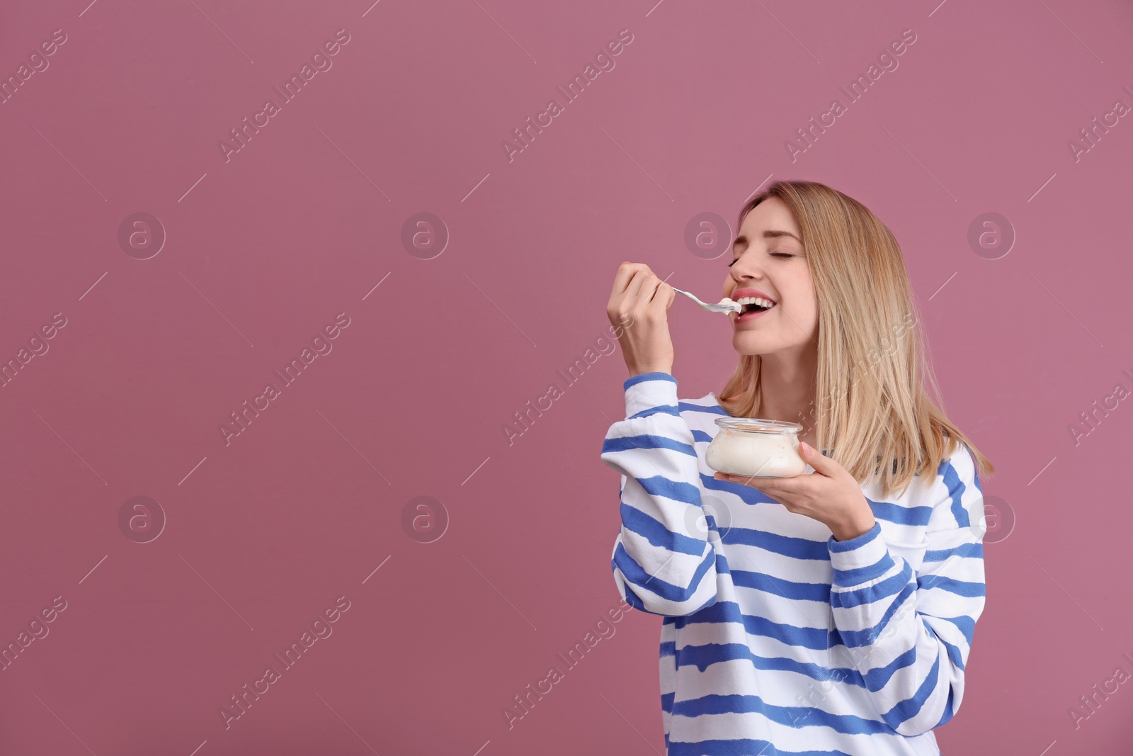 Photo of Young attractive woman eating tasty yogurt on color background