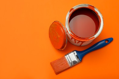 Photo of Can of orange paint and brush on color background, top view. Space for text