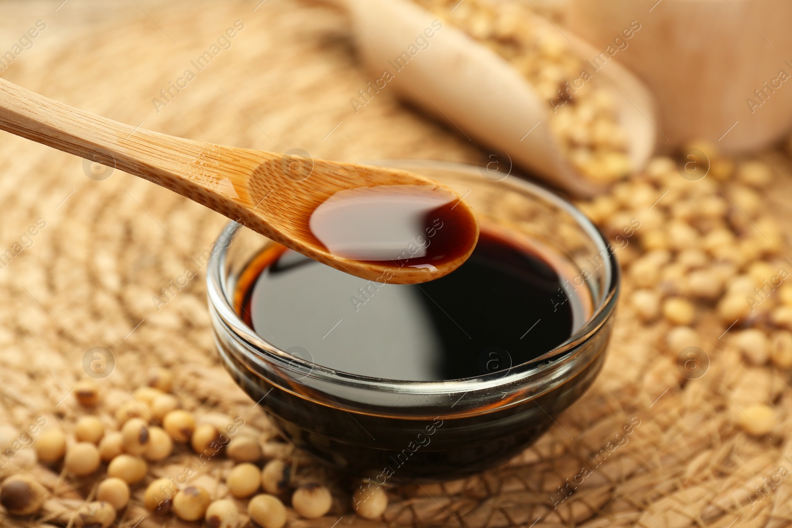 Photo of Taking soy sauce with spoon from bowl at table, closeup