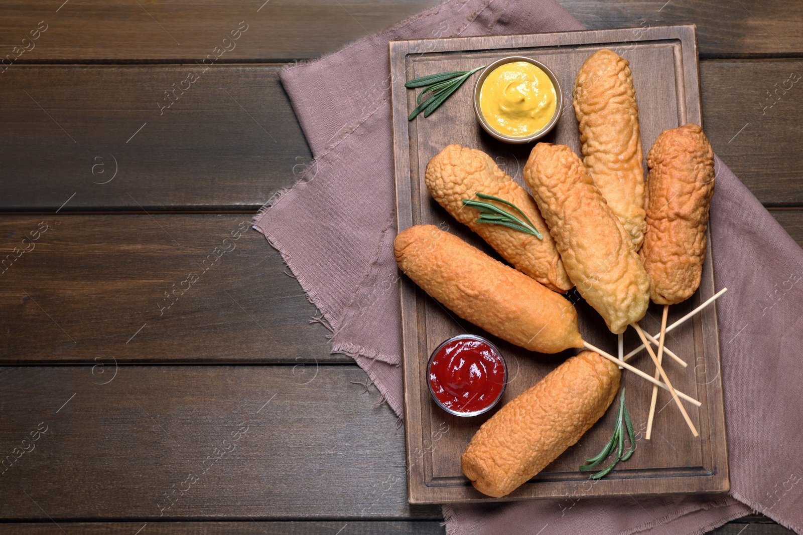 Photo of Delicious deep fried corn dogs with sauces on wooden table, flat lay. Space for text