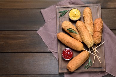 Photo of Delicious deep fried corn dogs with sauces on wooden table, flat lay. Space for text