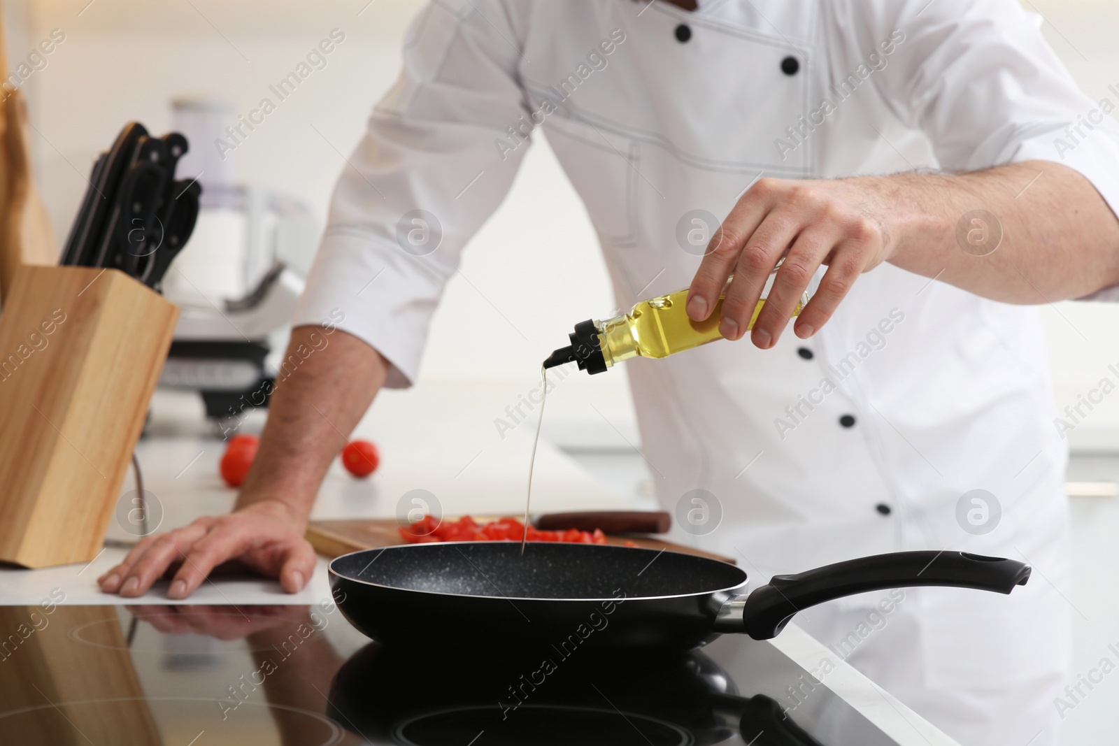 Photo of Chef pouring oil from bottle into frying pan indoors, closeup