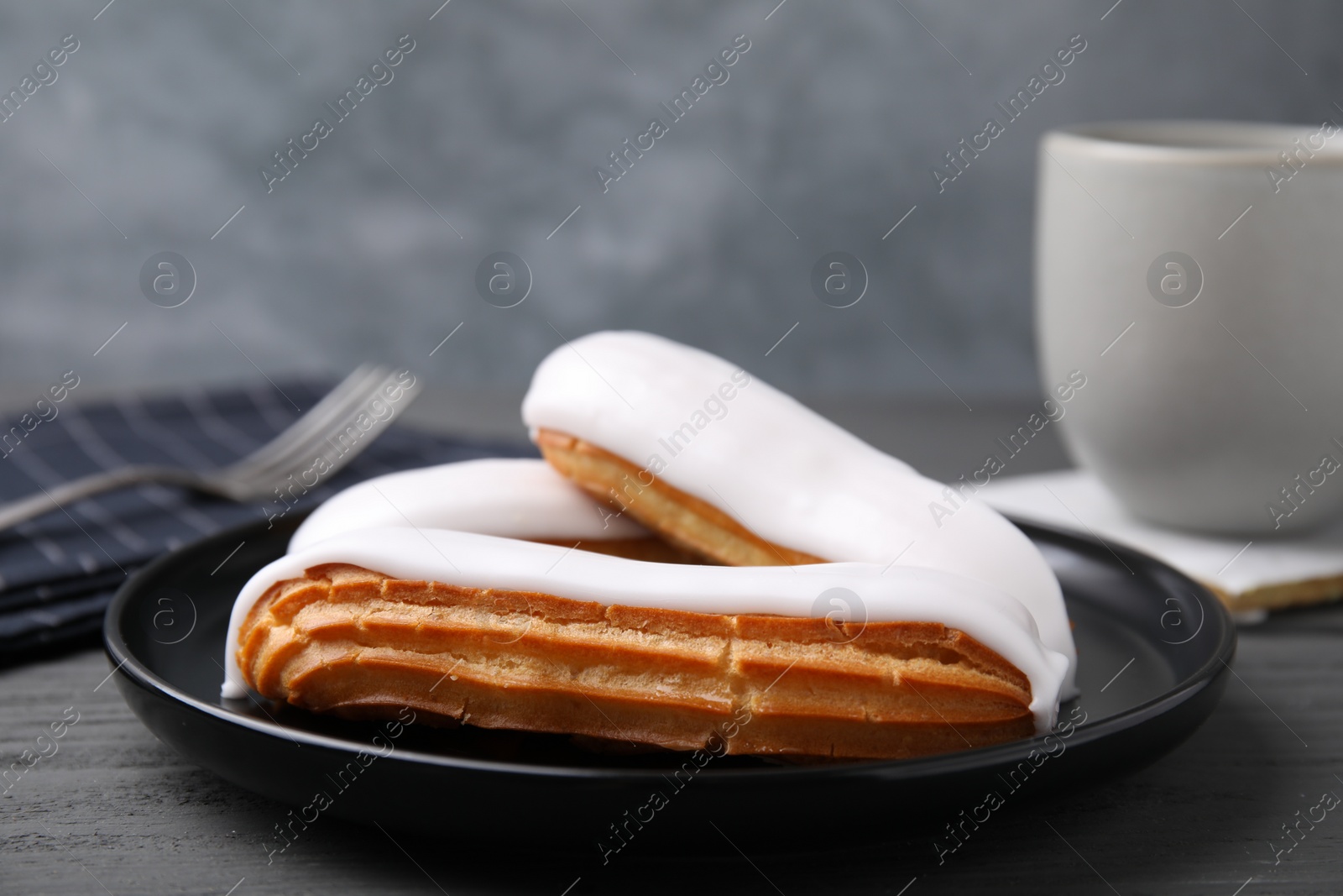 Photo of Delicious eclairs covered with glaze on grey wooden table, closeup