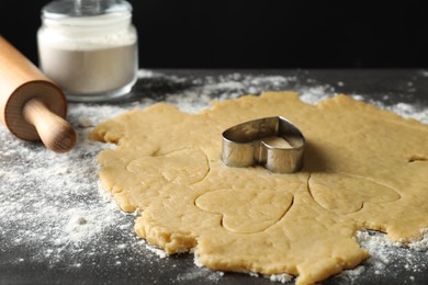 Photo of Making shortcrust pastry. Raw dough, flour, cookie cutter and rolling pin on grey table, closeup