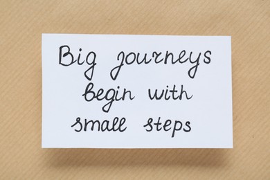 Photo of Card with phrase Big Journeys Begin With Small Steps on beige background, top view. Motivational quote