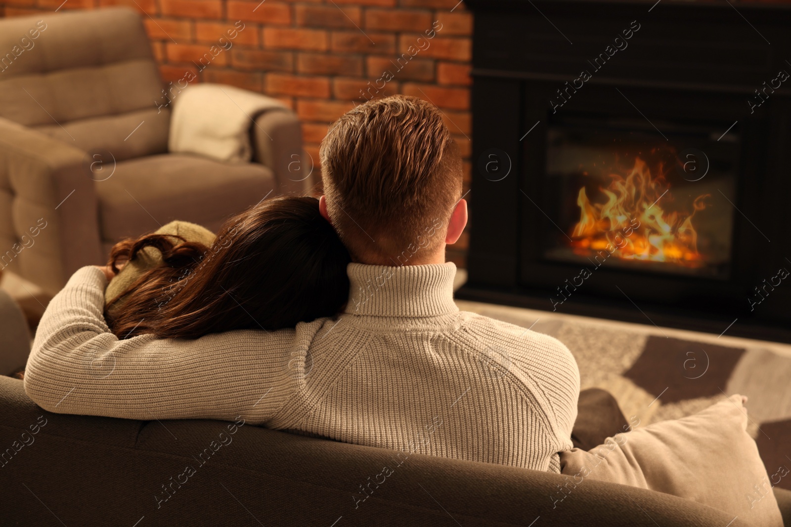 Photo of Lovely couple spending time together near fireplace at home, back view