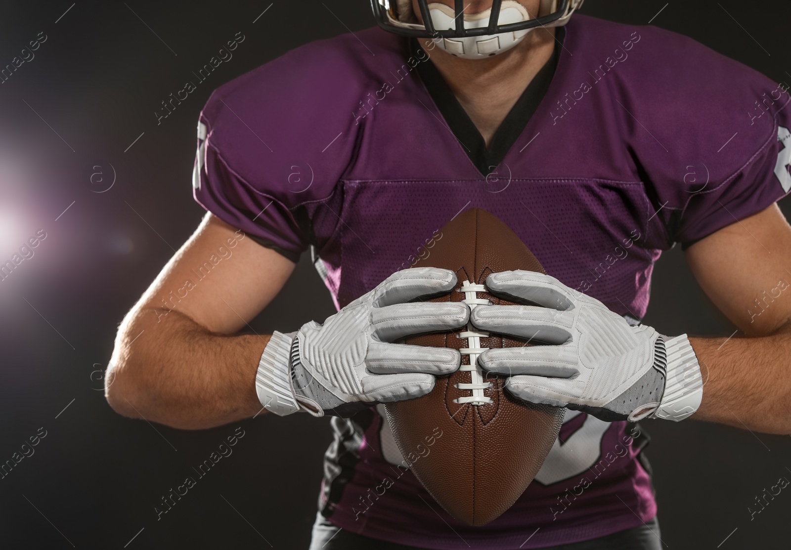 Photo of American football player with ball on dark background, closeup