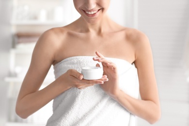 Photo of Young woman with jar of body cream at home