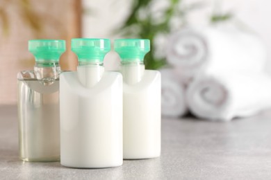 Photo of Mini bottles of cosmetic products on light grey table against blurred background. Space for text