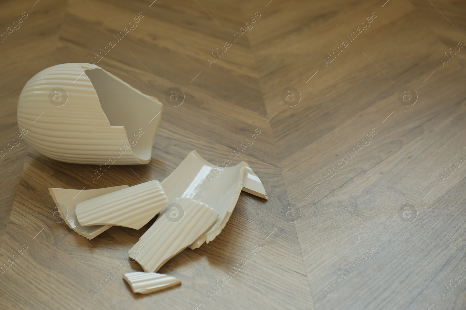 Photo of Broken white ceramic vase on wooden floor. Space for text