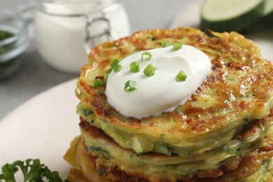 Delicious zucchini fritters with sour cream on plate, closeup view