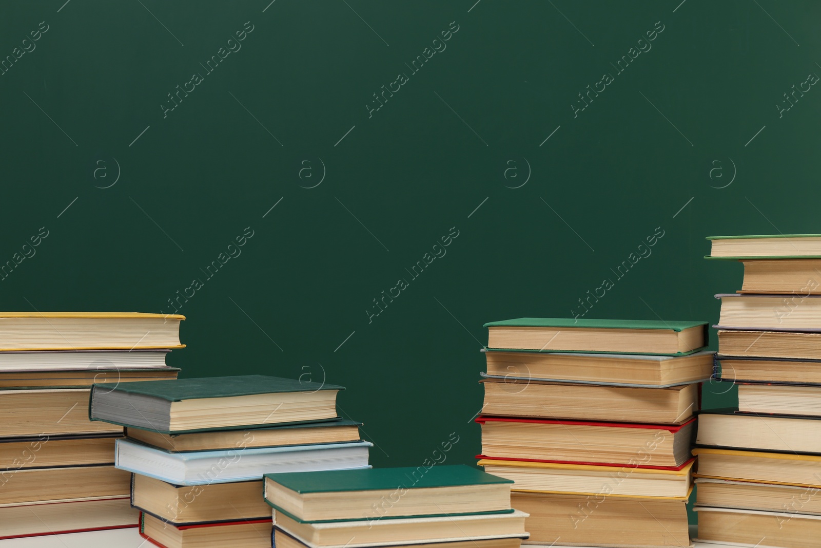 Photo of Many hardcover books near green chalkboard, space for text. Library material