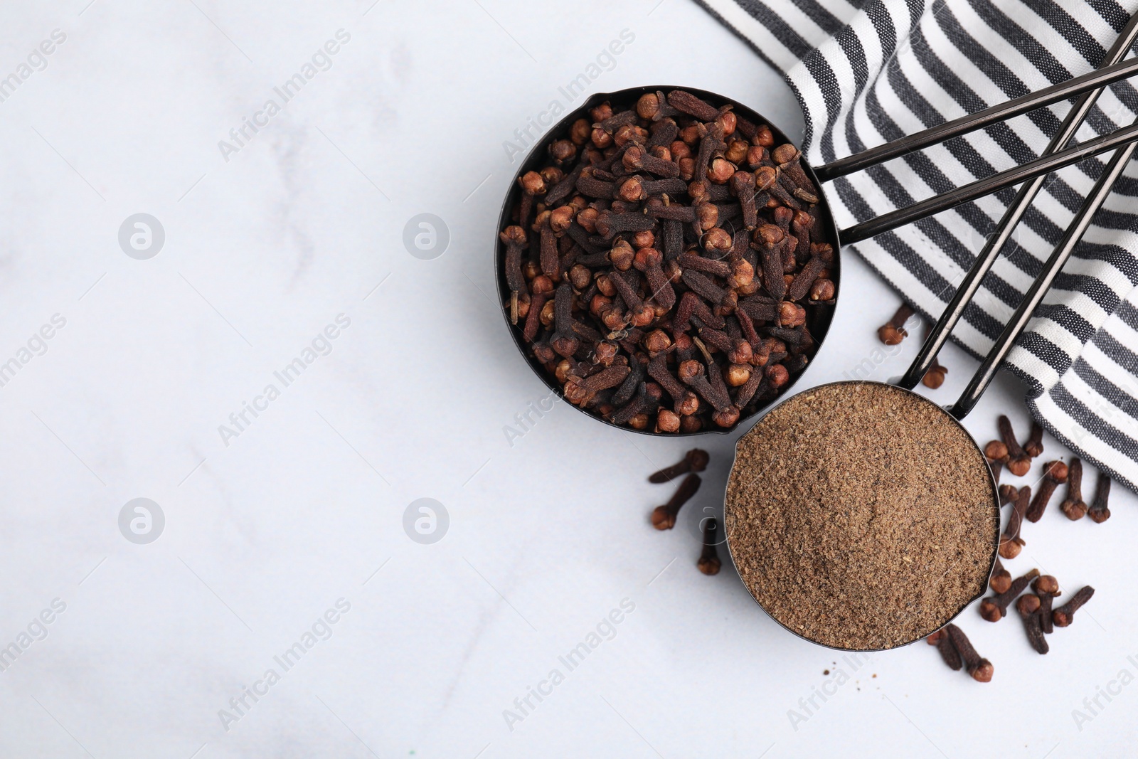 Photo of Aromatic clove powder and dried buds in scoops on white table, top view. Space for text